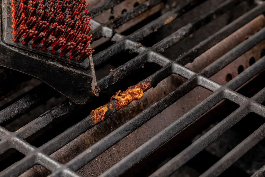 Close up of a grill brush scrubbing food residue Close up of a grill brush scrubbing food residue from dirty grill grates to show how to clean a grill safely.