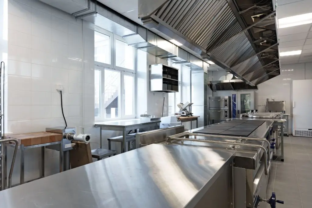 Professional workspace showing stainless appliances in kitchen with vent hoods and prep tables Professional workspace showing stainless appliances in kitchen with vent hoods and prep tables.