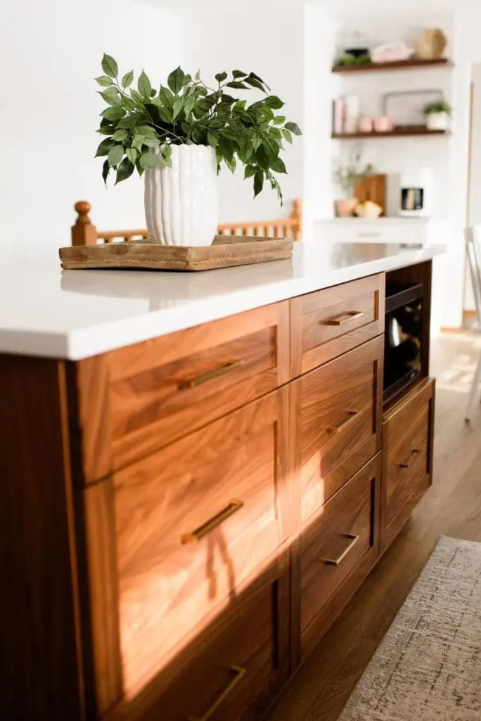Warm modern kitchen island with wood cabinetry featuring a built-in microwave drawer in island design