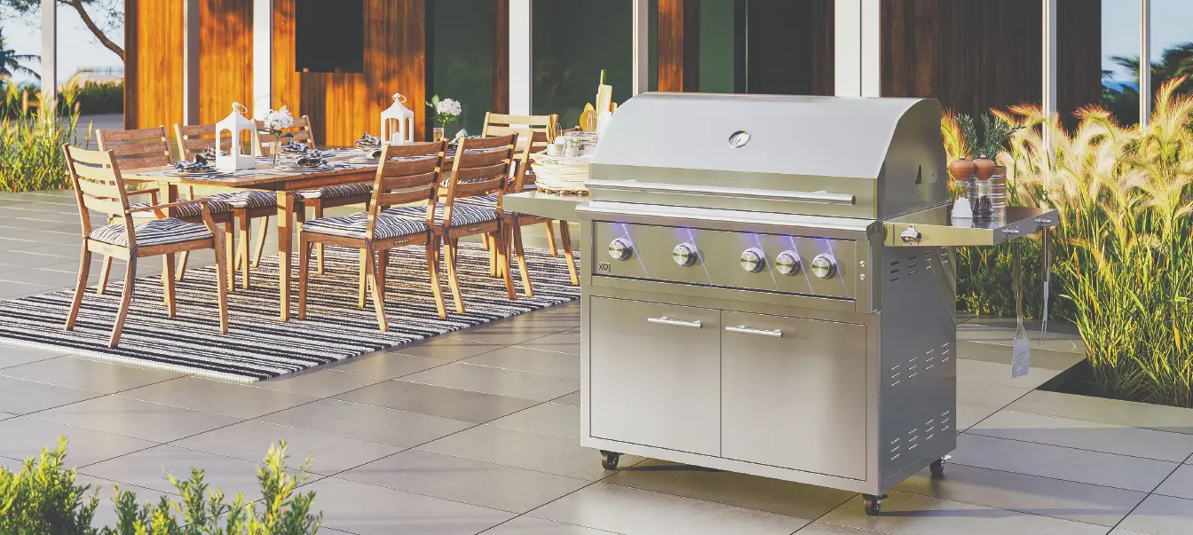 XO Pro-Grade grill on a stainless steel cart beside an outdoor dining area